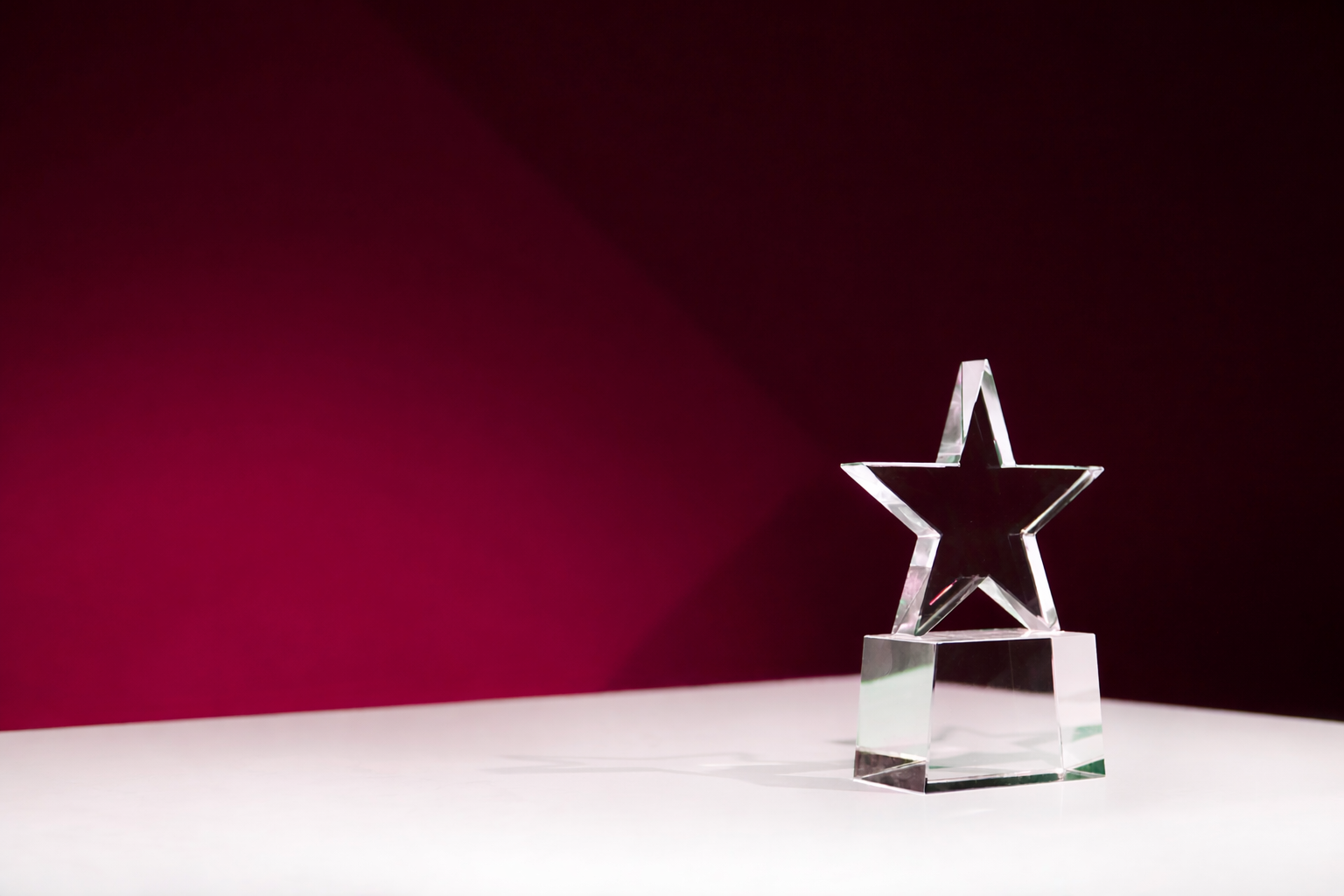 Clear star-shaped trophy on a white surface with a dark red background